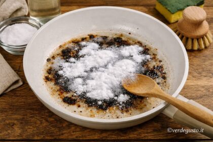 Padella in ceramica con residui bruciati pulita con bicarbonato e acqua su tavolo in legno - Foto Vgai