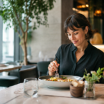Donna che mangia da sola in un ristorante moderno, simbolo della crescita del solo dining e dei nuovi comportamenti nella ristorazione. Foto vgai